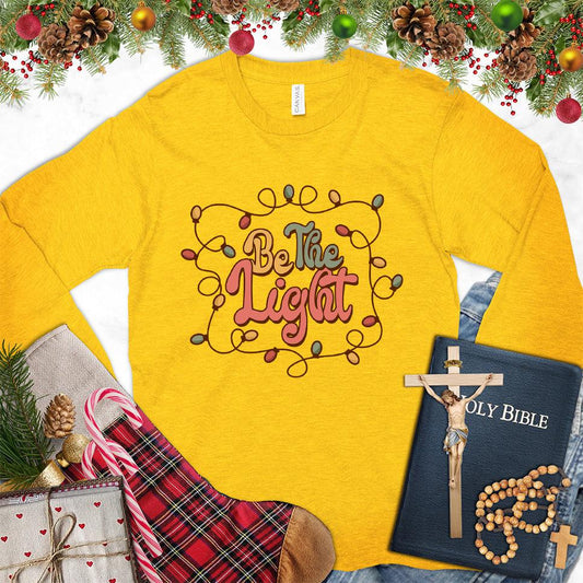 Be The Light Colored Edition Long Sleeves Gold - Inspiring 'Be The Light' design on a long sleeve tee with cozy holiday vibes.
