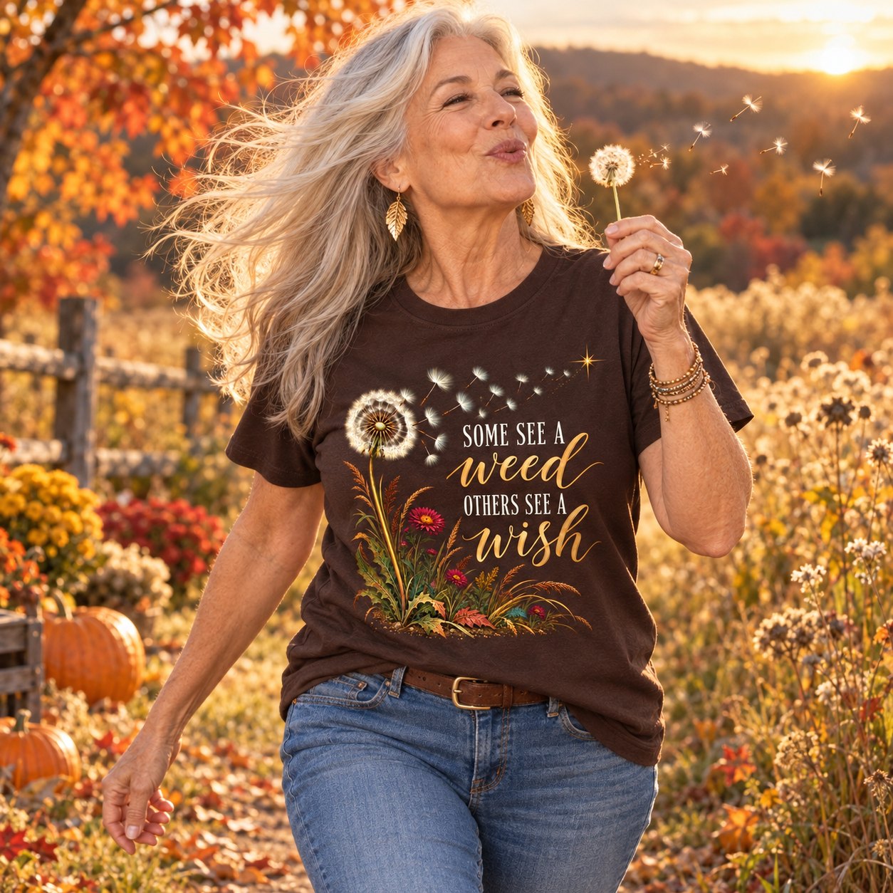 A woman in her 60s blowing a dandelion in an autumn meadow in the Some See A Weed shirt